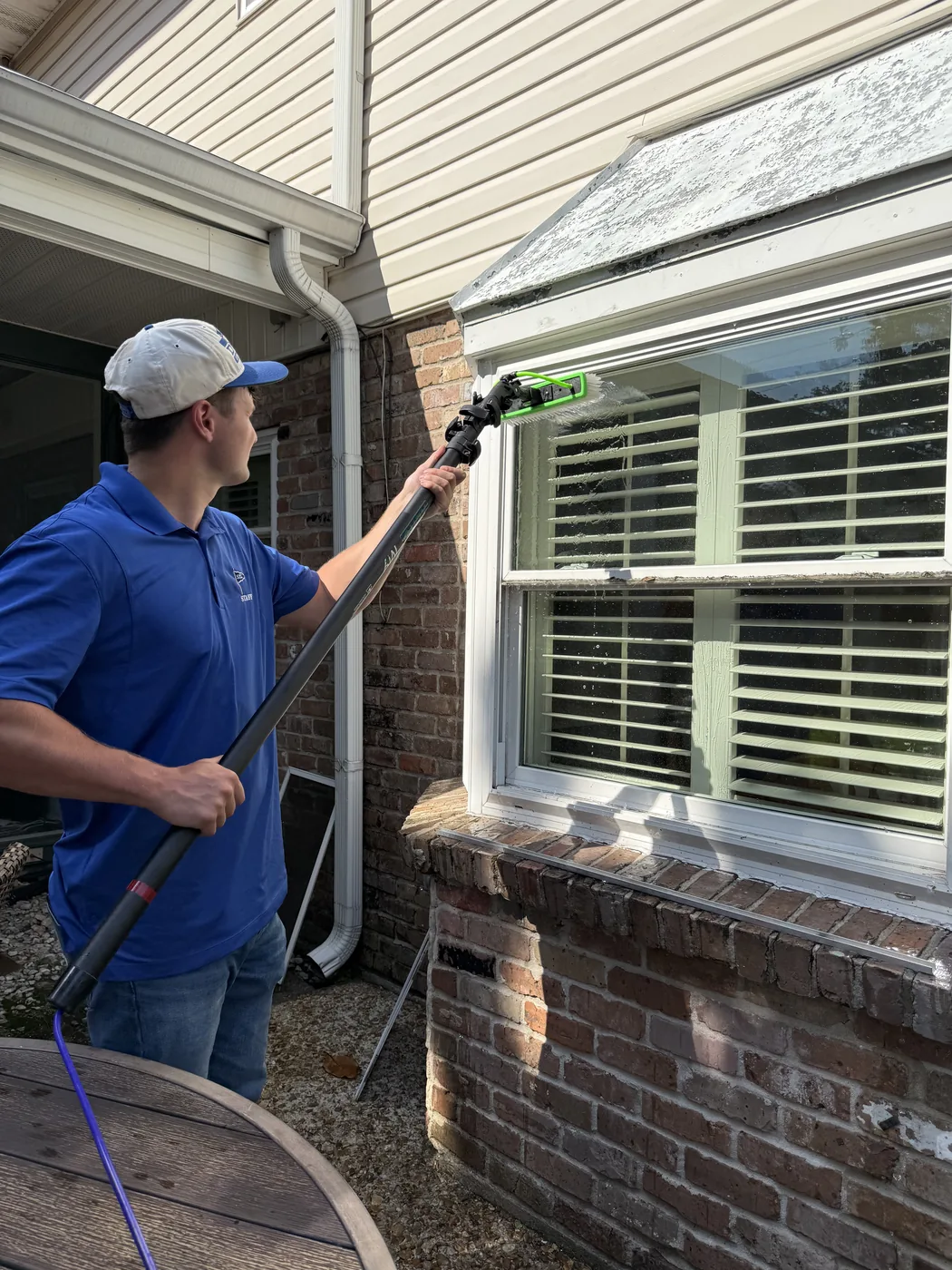 Boot Krewe Cleaners technician in a company polo cleaning a window on a brick house