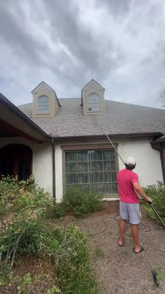 Technician cleaning upper windows on a stucco house with a water fed pole