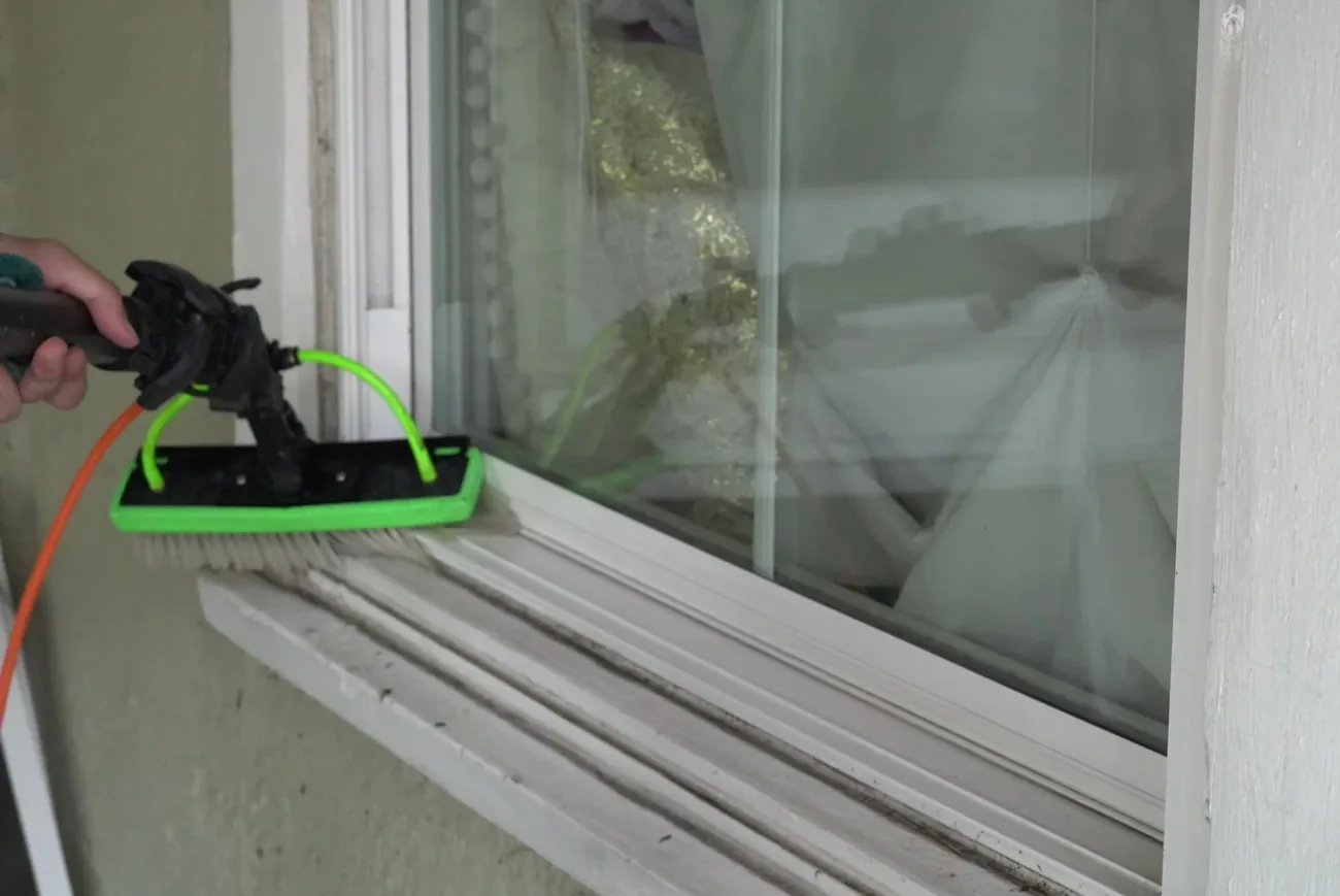 Close-up of the green pure-water brush head resting on a weathered white window sill with the orange hose attached