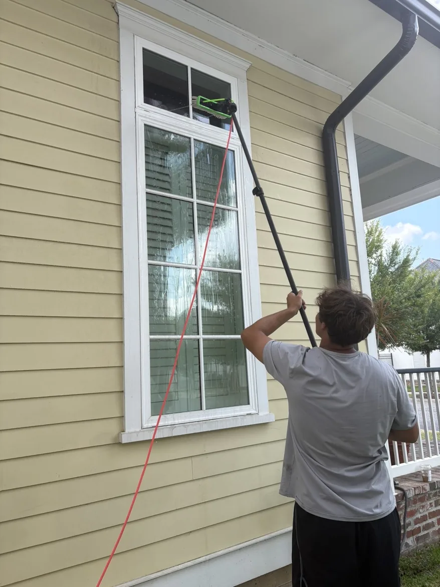 Technician reaching a sash window on yellow clapboard siding with a water fed pole