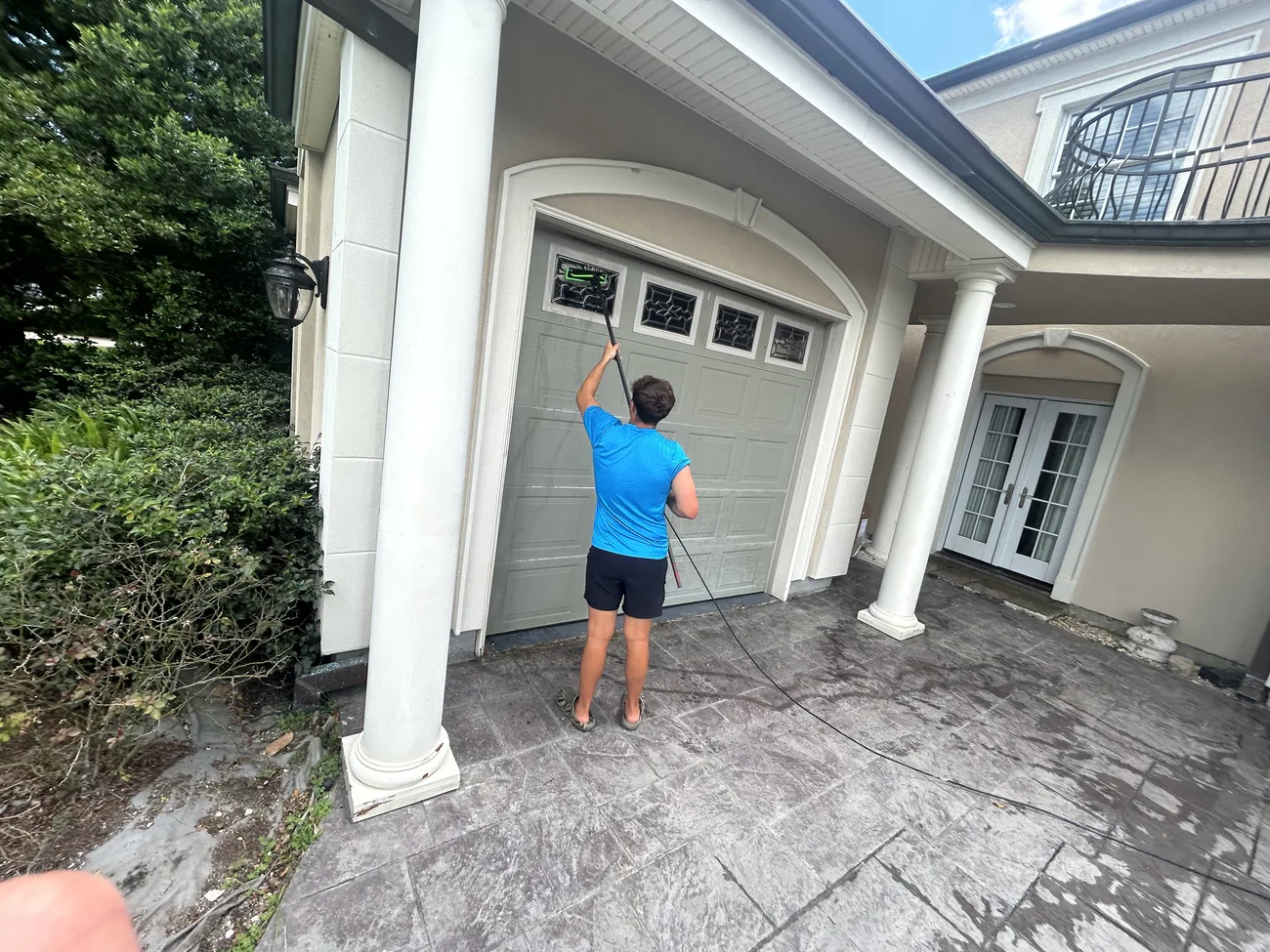 Technician in a Boot Krewe shirt running a water fed pole across transom windows above a garage door
