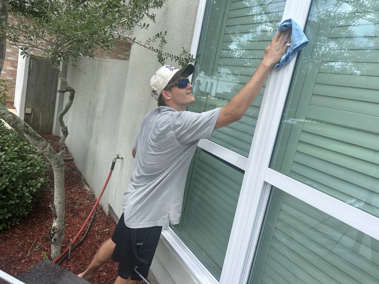 Boot Krewe technician in a branded cap wiping a large pane with a blue microfiber cloth