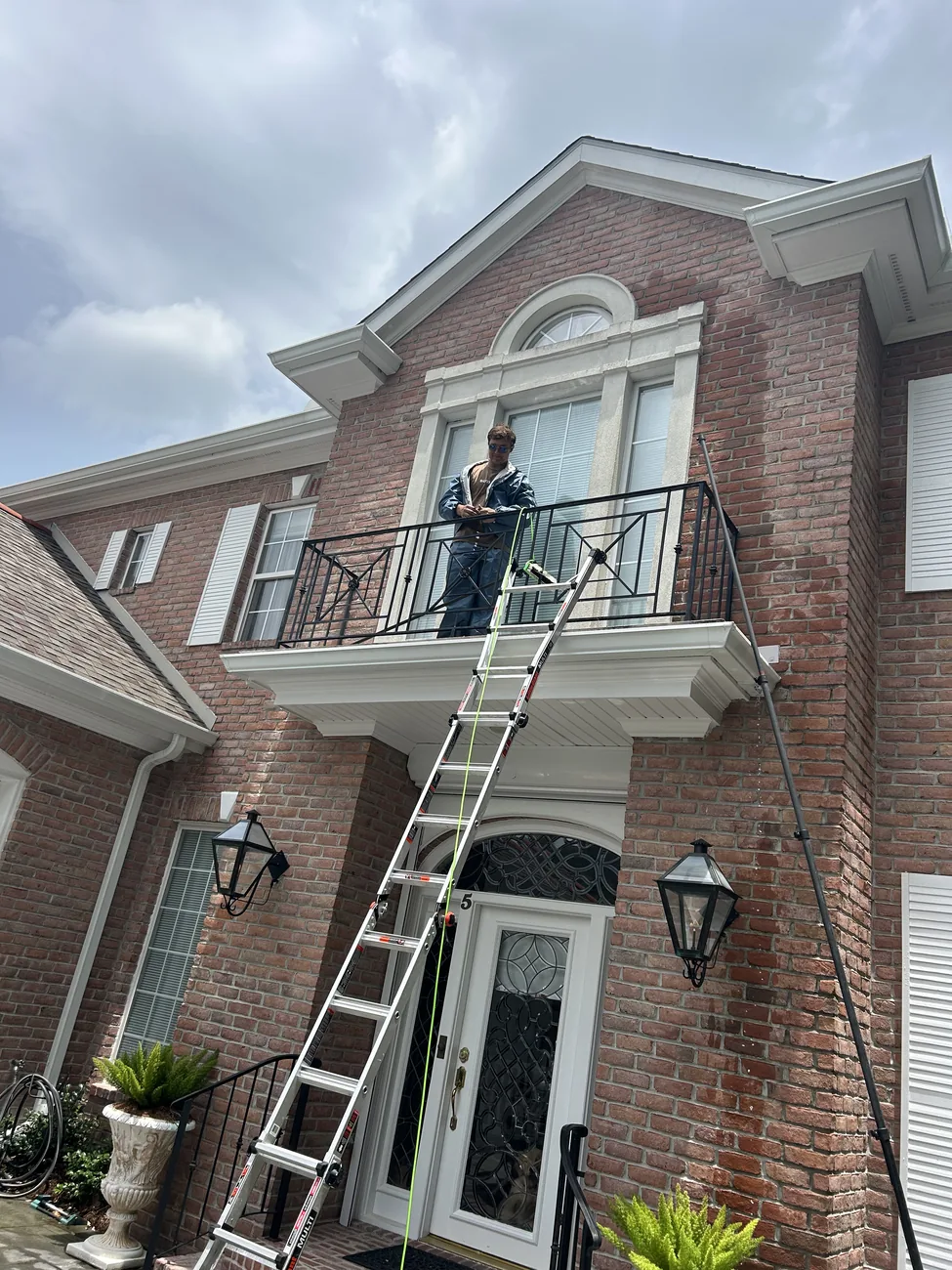 Extension ladder reaching a second storey balcony on a brick house while a technician works above