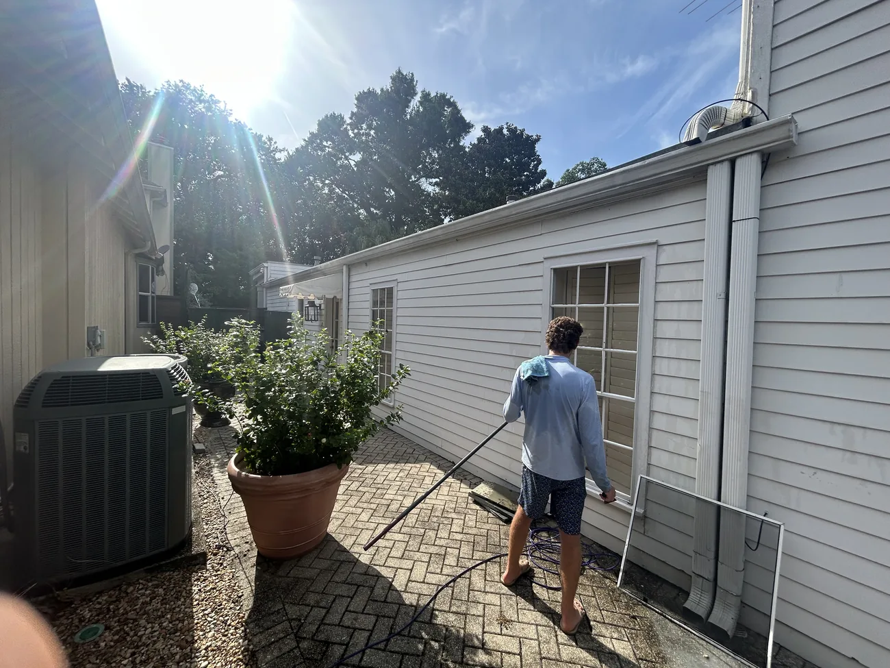 Boot Krewe technician carrying a water fed pole along the side of a house in the sun