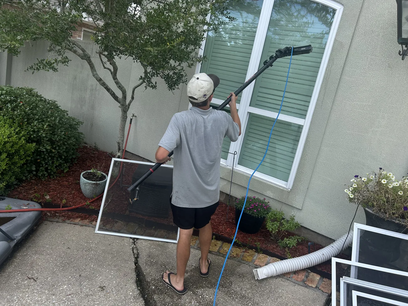 Window screens leaning against a wall while a technician cleans the glass with a water fed pole