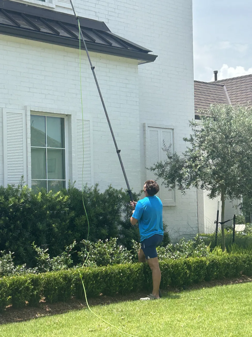 Technician with a tall water fed pole cleaning upper windows on a white brick house